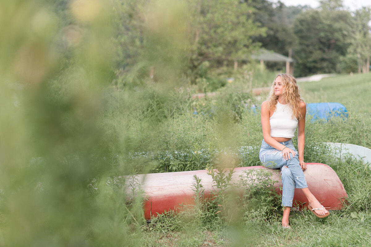 Senior girl sitting on red canoe looking right with legs crossed at Speedwell Forge Lake .