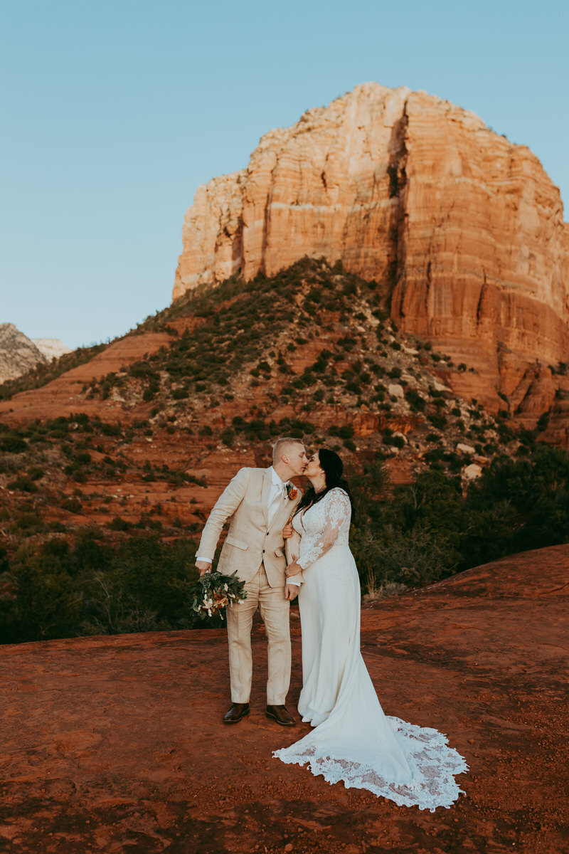 Bridal couple kisses with courthouse vista behind them in sedona