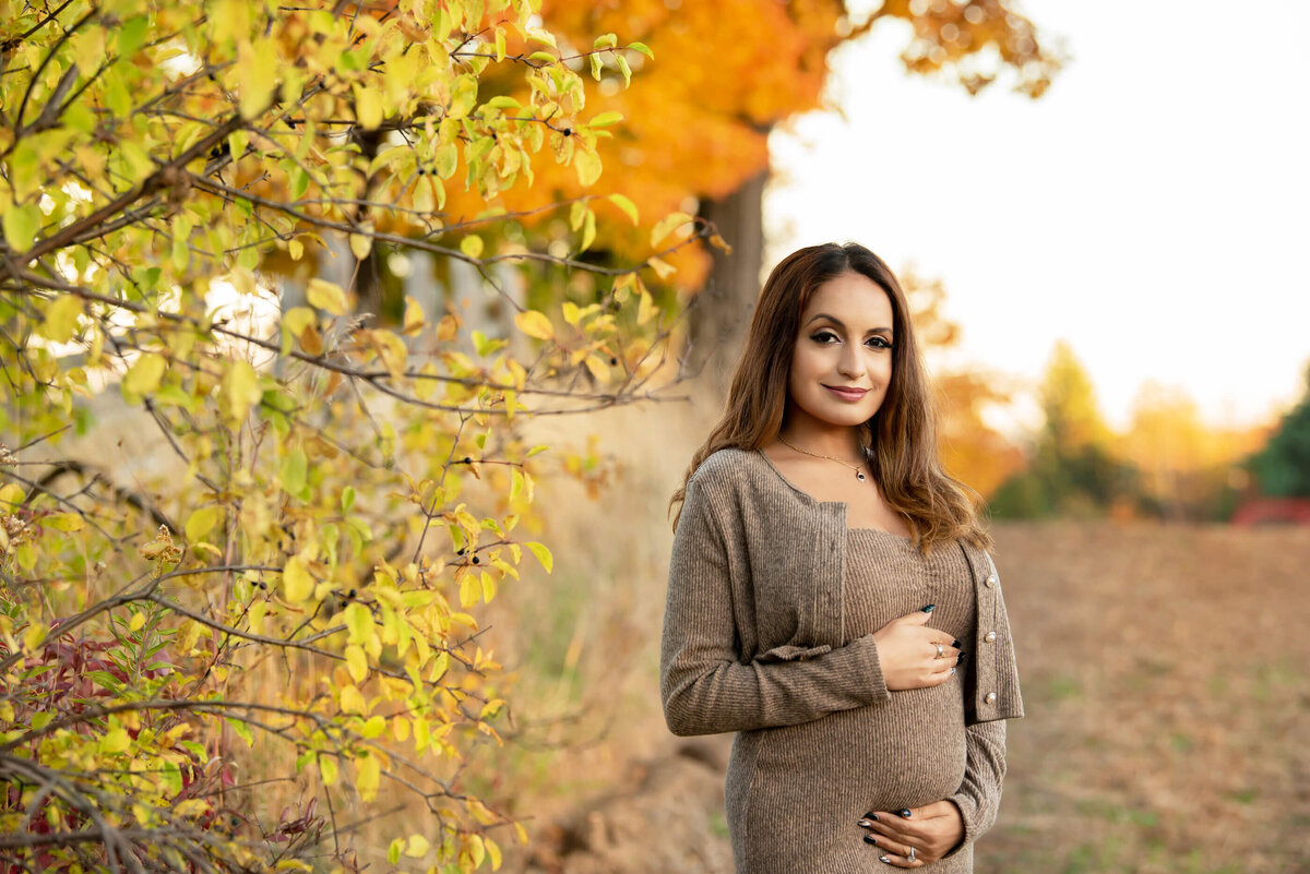 pregnant woman wearing a beige dress for her fall maternity photos in Burlington