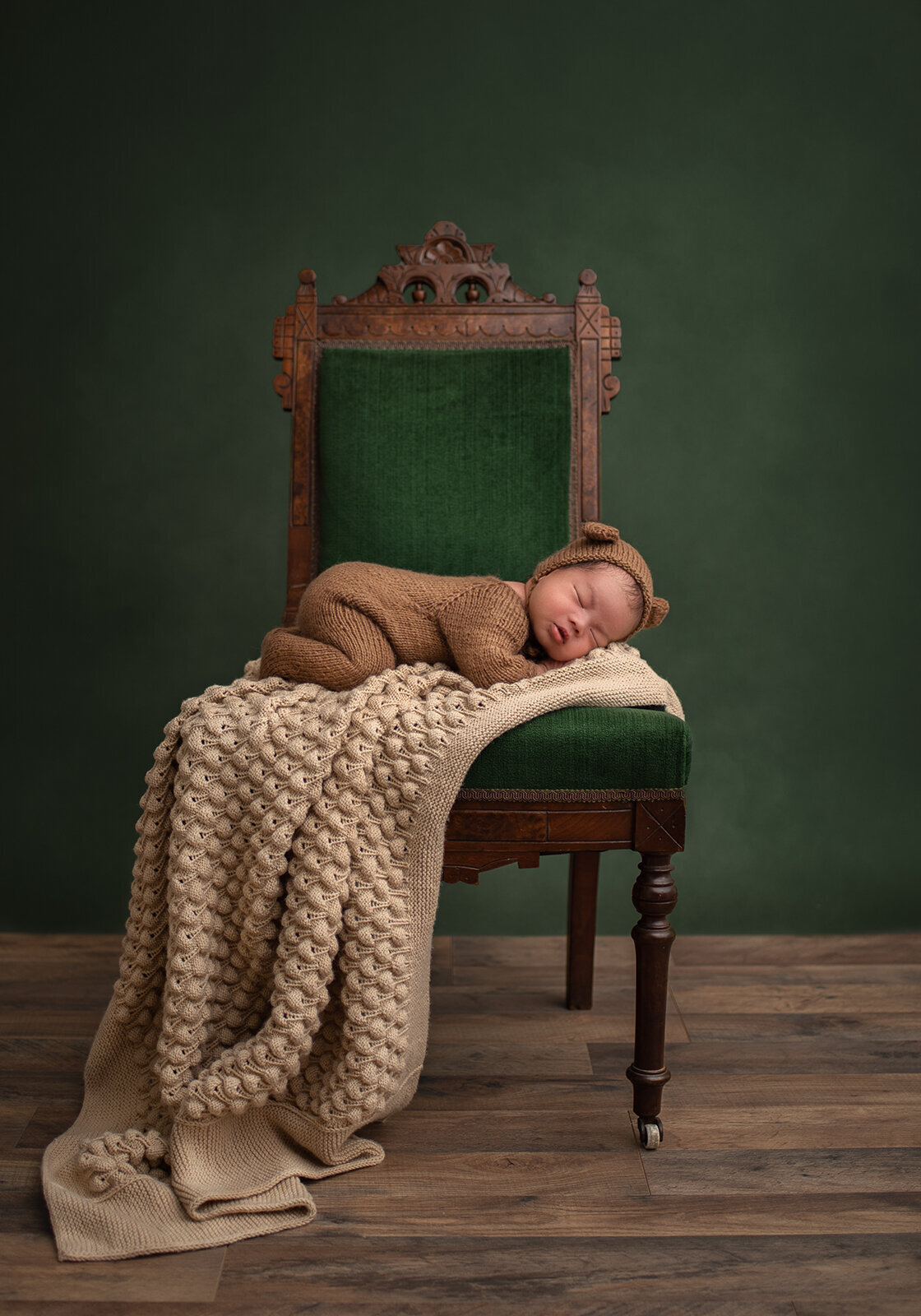 baby sleeping on chair with tan blanket and green background