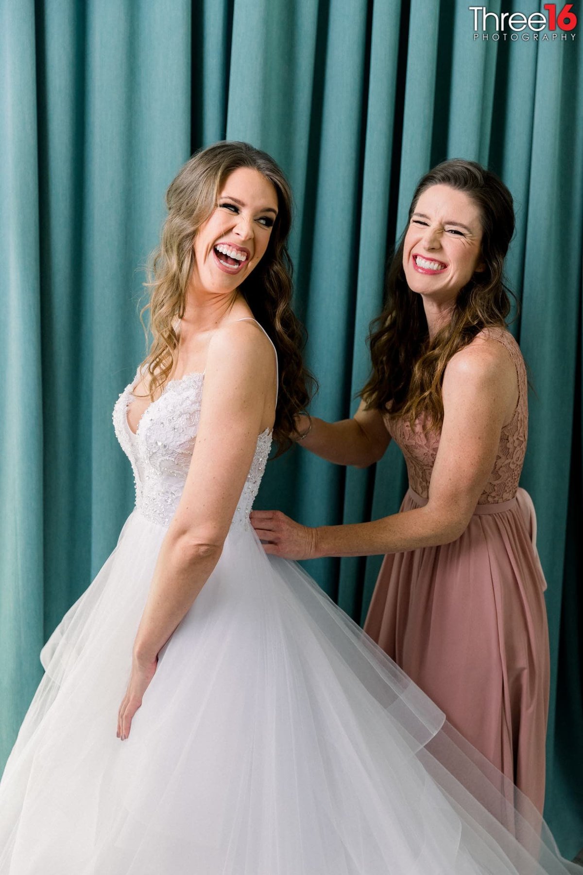 Bride and Maid of Honor share a laugh while Bride's dress is being buttoned up