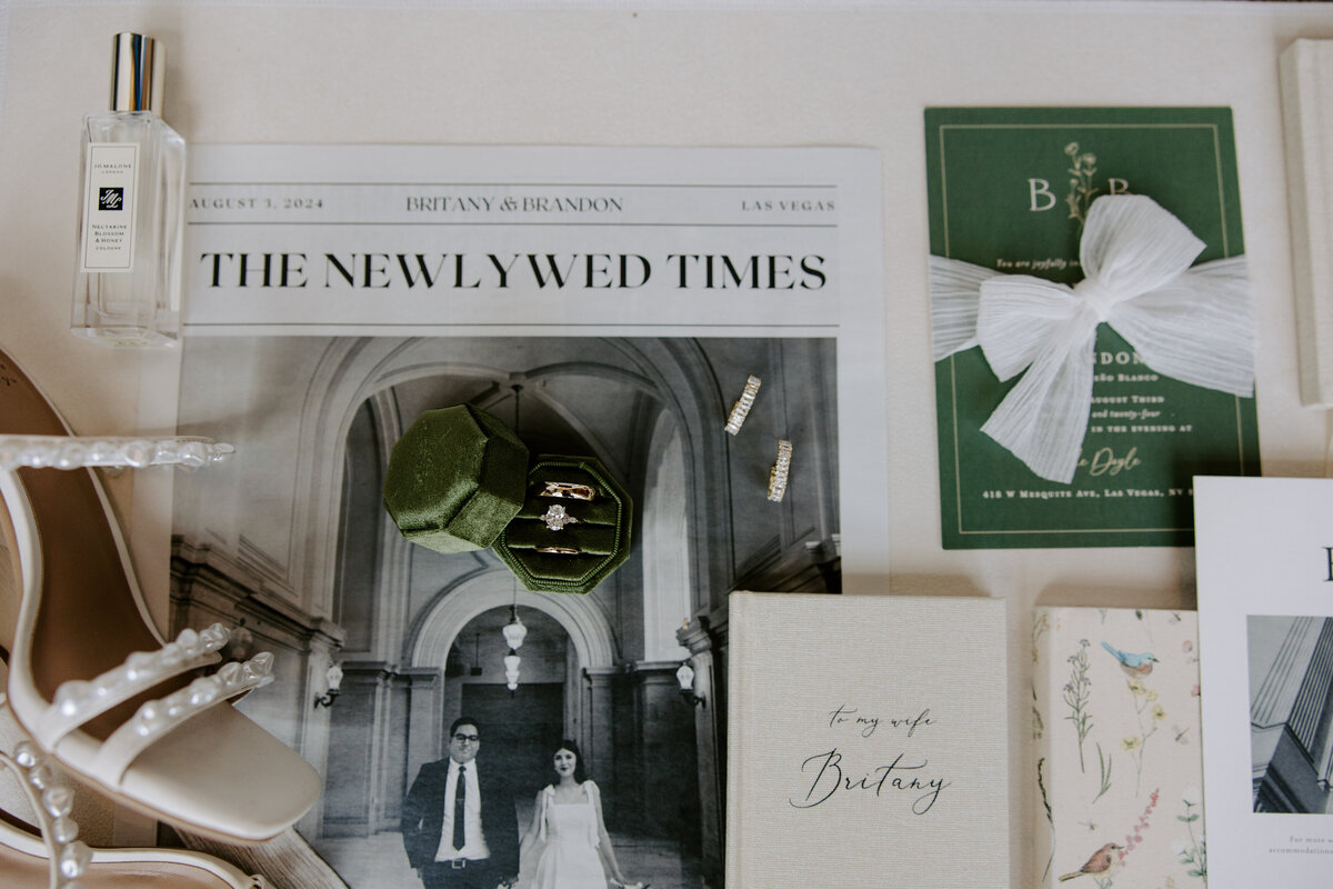 Close up of details from a wedding featuring stationary, a ring box, and The Newlywed Times.