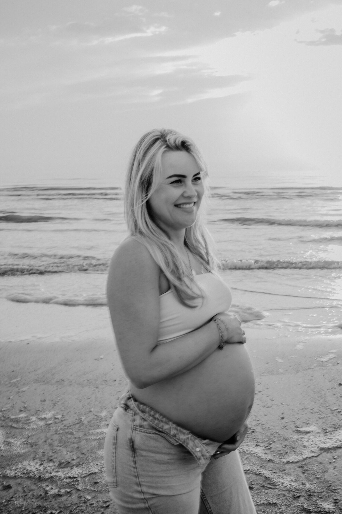 Zwangere vrouw lacht tijdens zwangerschapsshoot aan het strand.