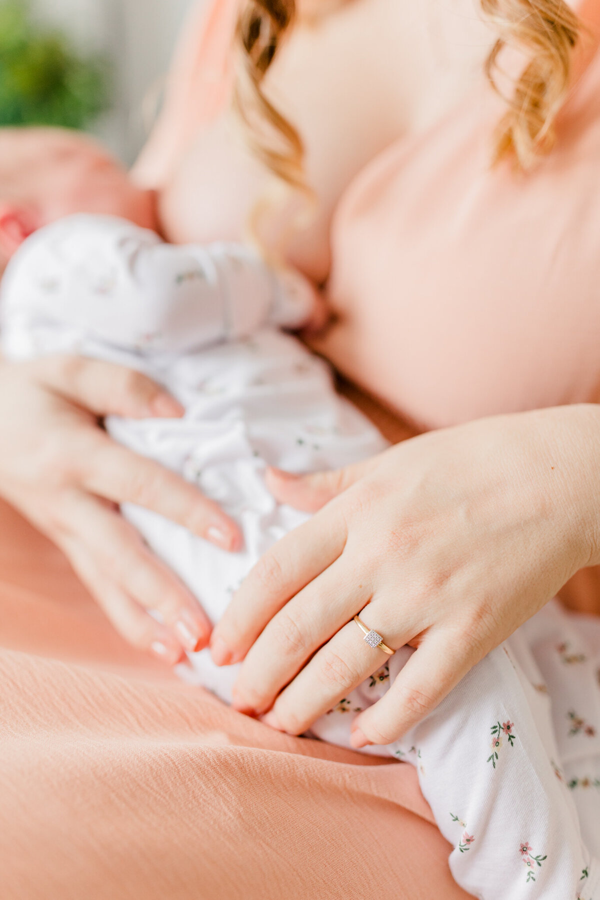 Focus of the image is on a mother's hand as she hold's her newborn in her lap to nurse