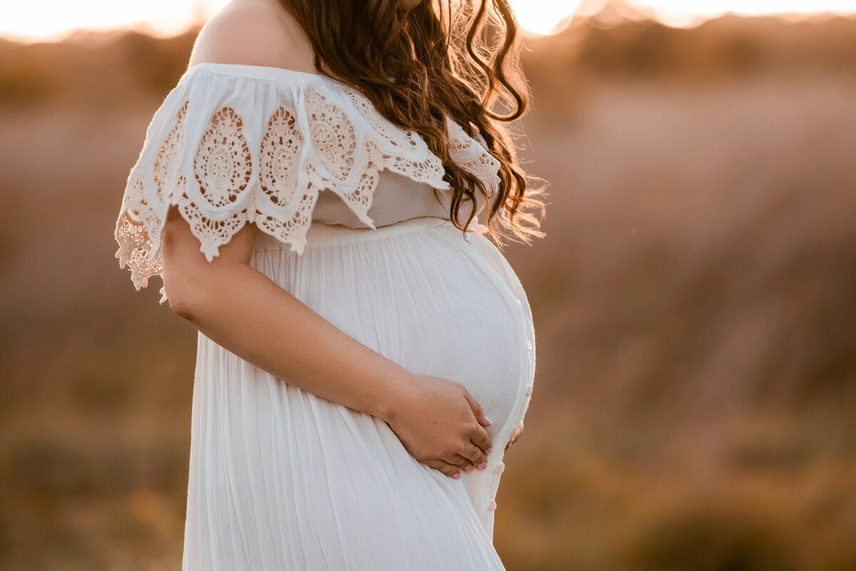 Maternity portrait of expectant mother in lace off-shoulder gown during golden hour photography session