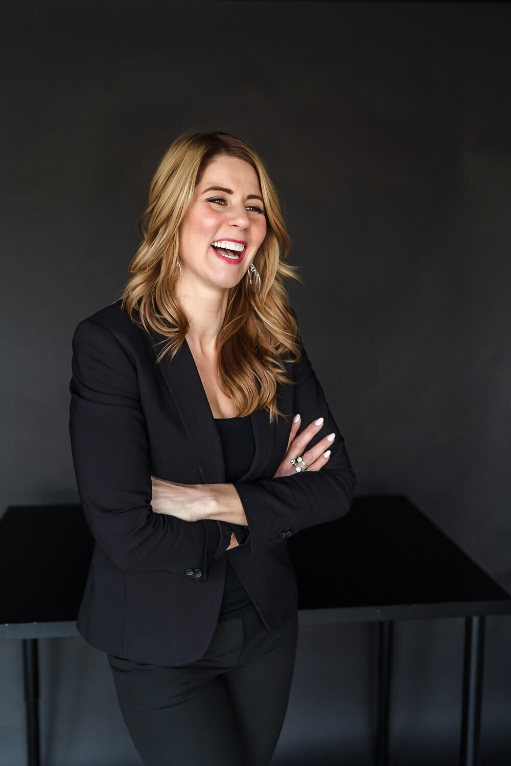 Smiling woman in black blazer standing with arms crossed in studio