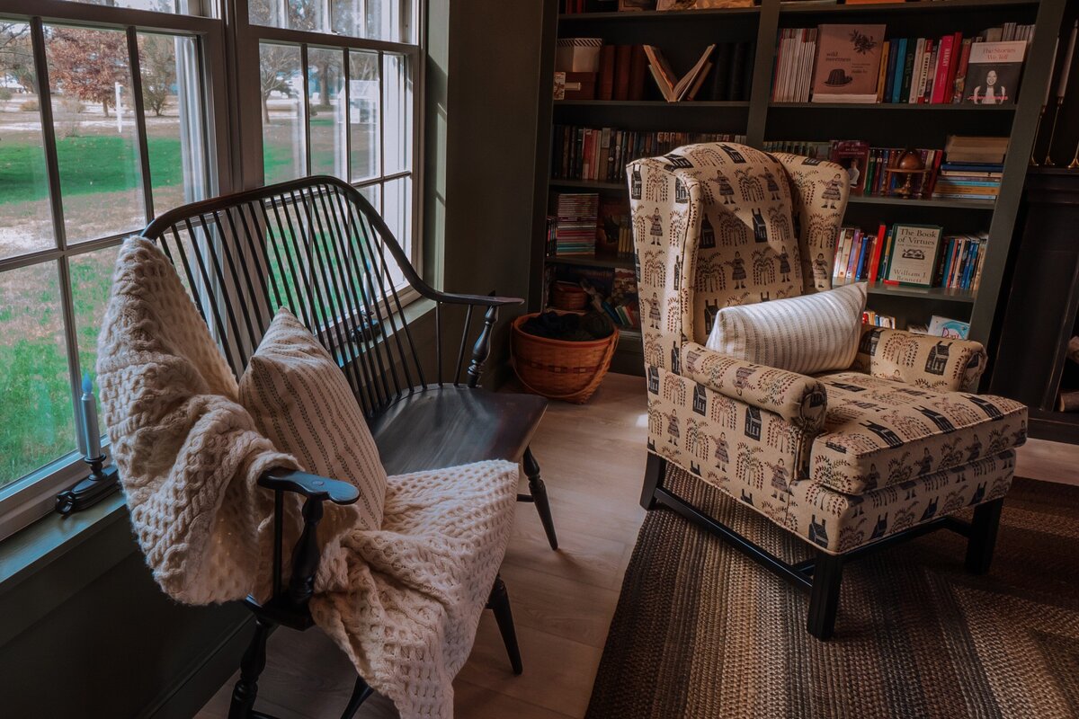 Cozy reading nook with antique spindle double seat wooden bench along with a wingback chair and a built-in  bookshelves holding piles and piles of books