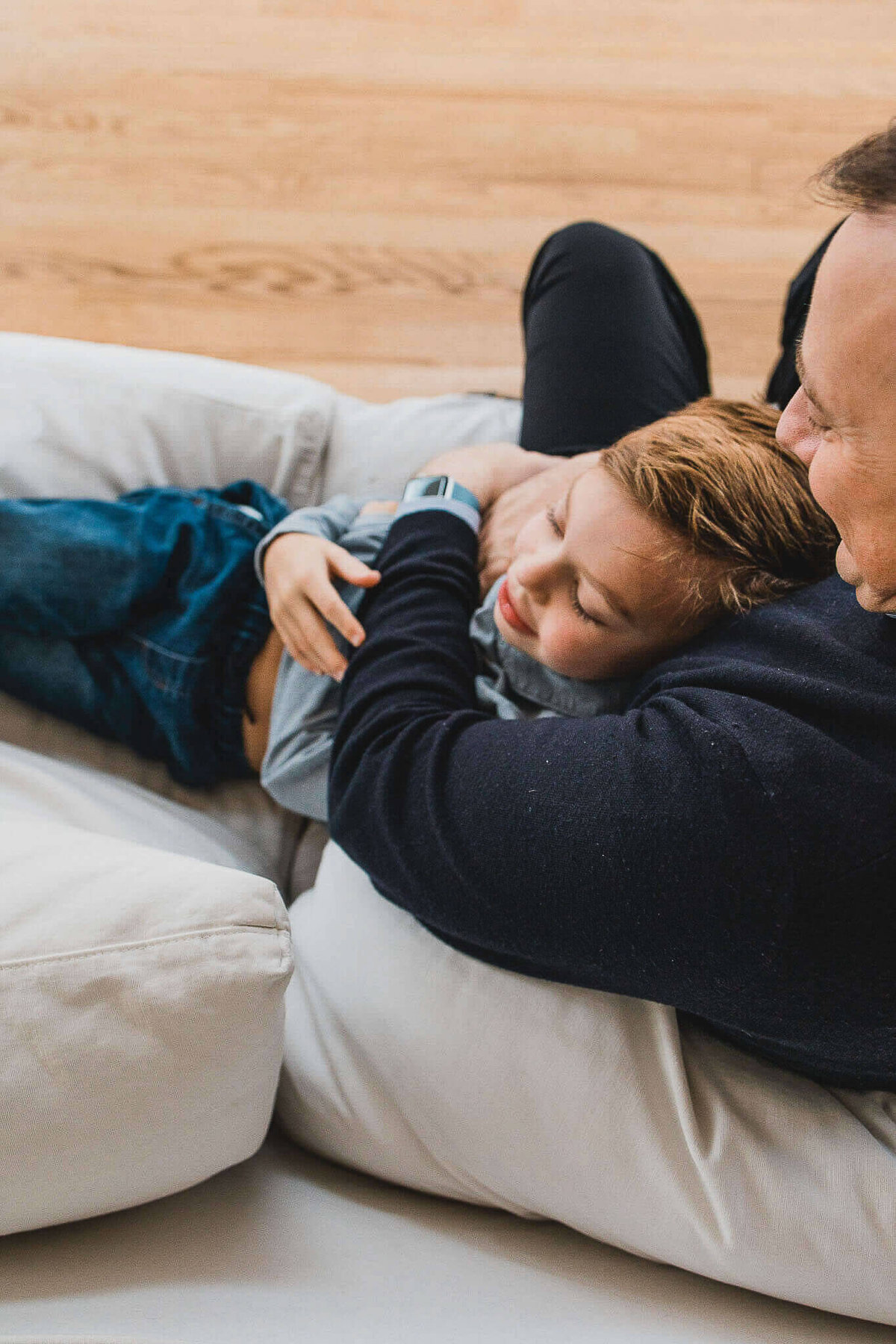 Father snuggling with son on white couch during Cleveland in-home photography session.