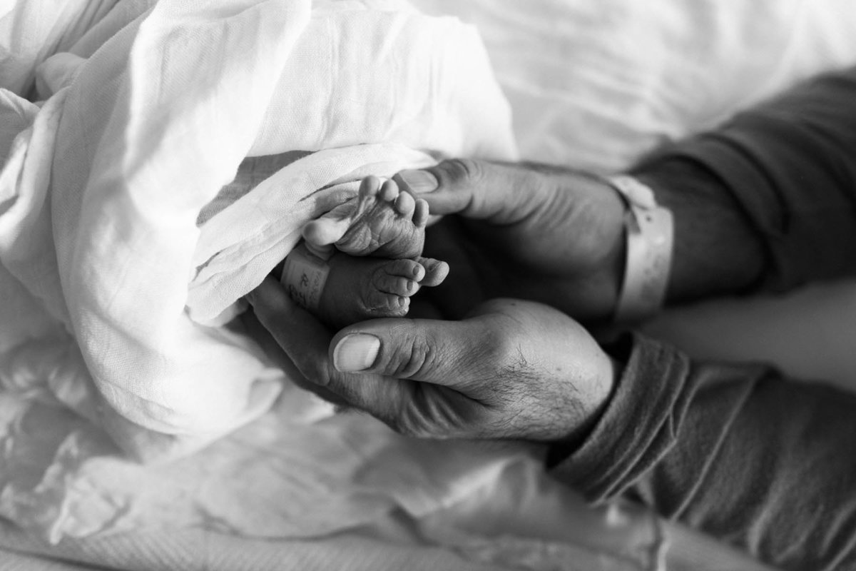Father holds newborn baby's feet at a hospital session by Laurie Baker