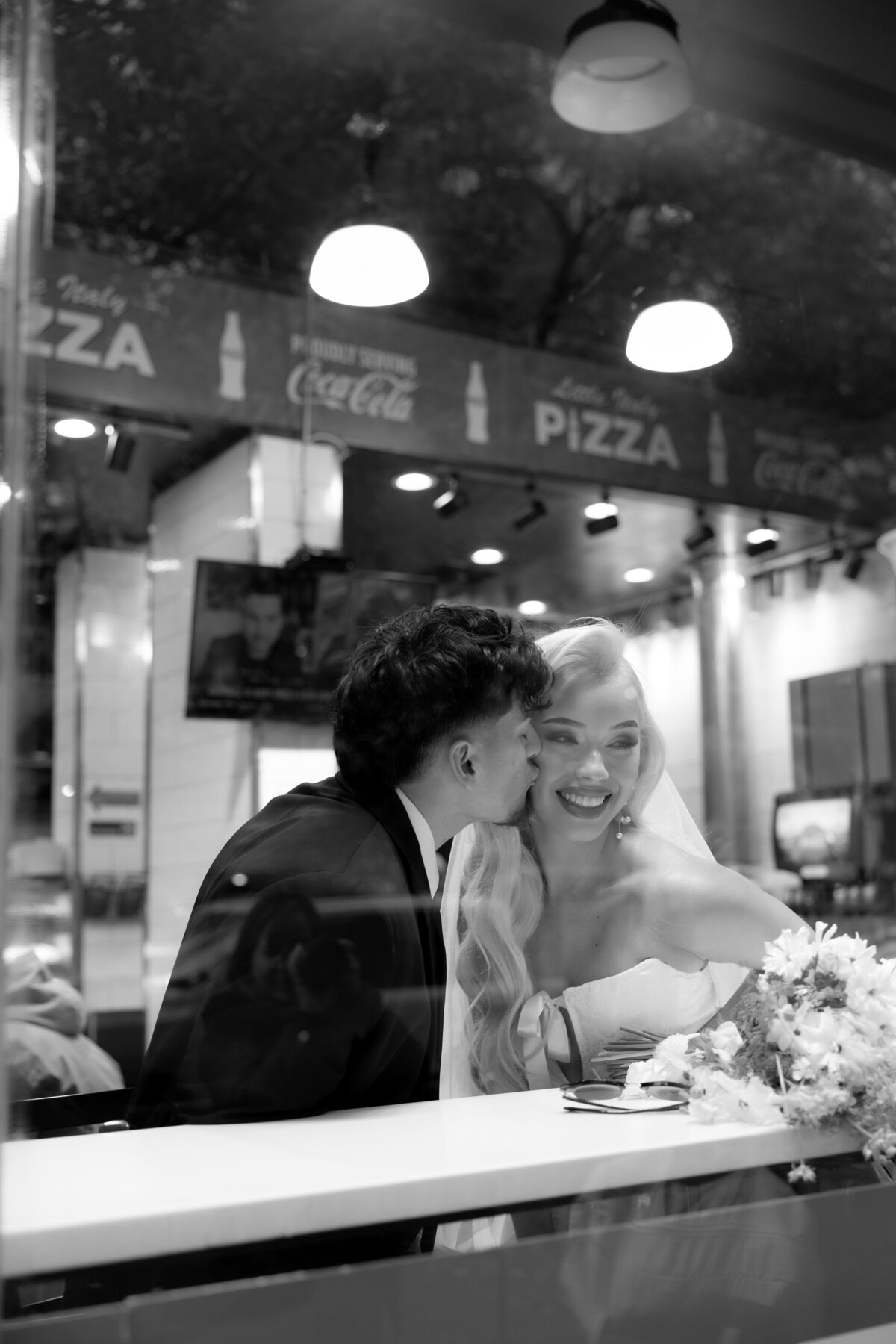 A candid moment of the couple chatting and eating pizza inside a busy NYC pizza shop.