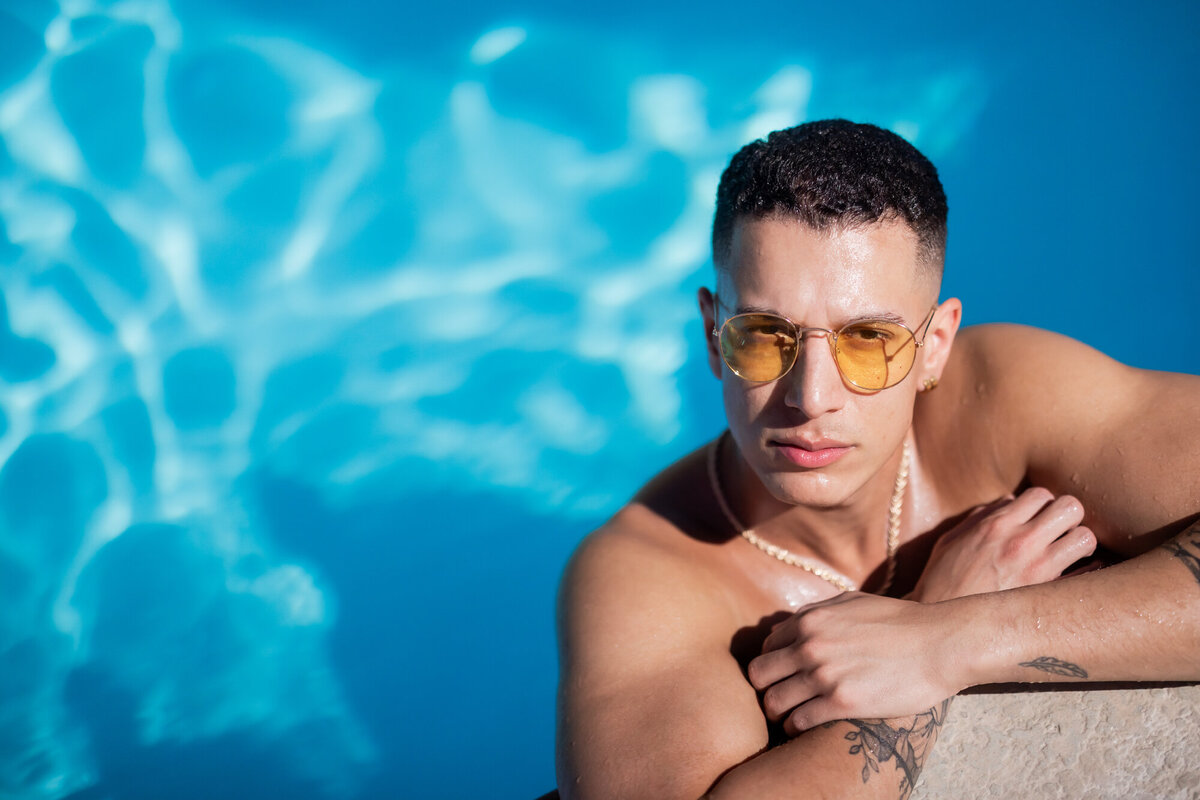 Close-up fashion portrait of model poolside, staring into the camera with strong light and saturated summer color.
