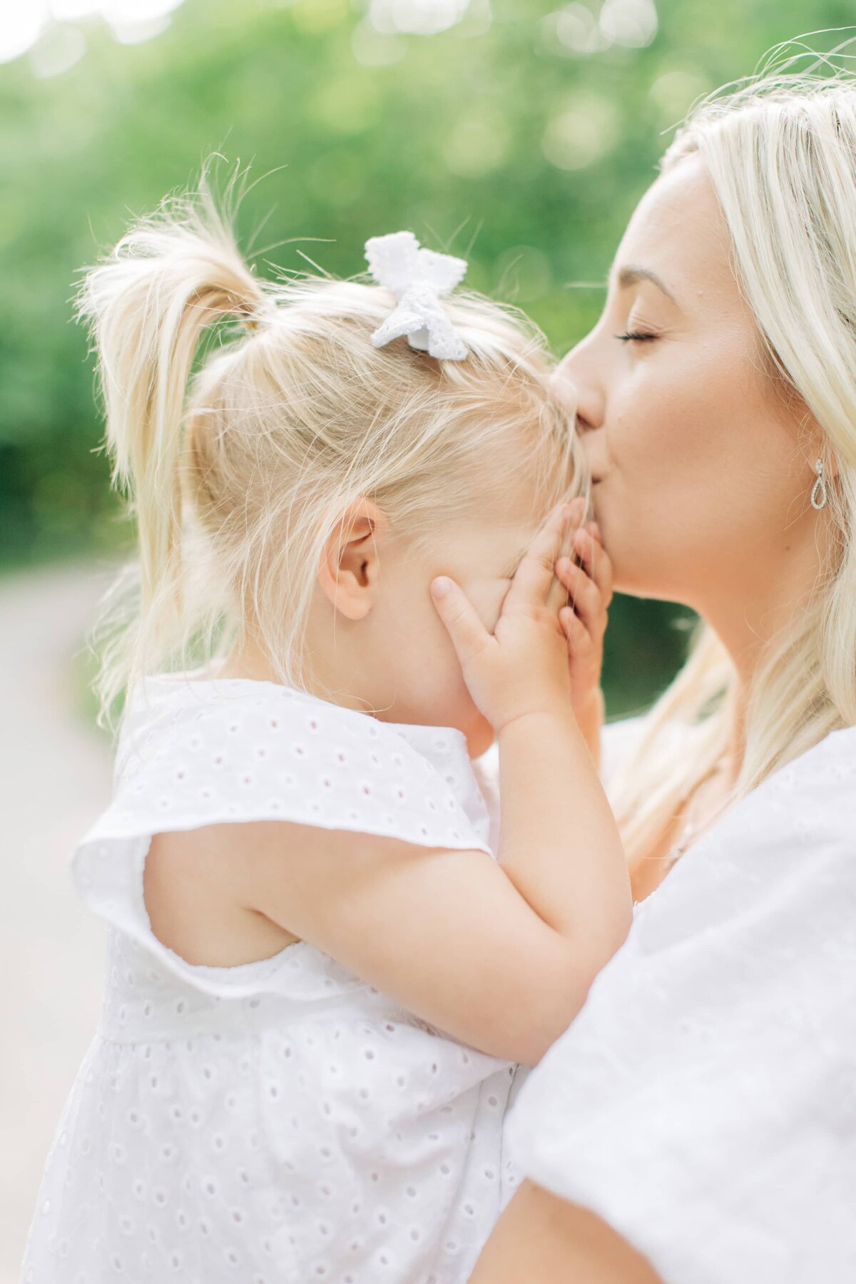 En dotter håller för ögonen och mamman pussar på hennes panna
