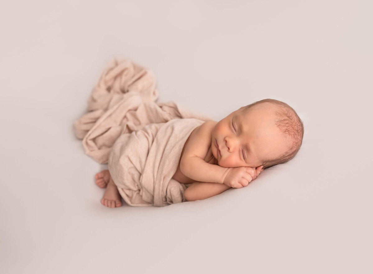 A tiny, newborn baby sleeps on a white blanket during his newborn session with an Asheville   Newborn Photographer