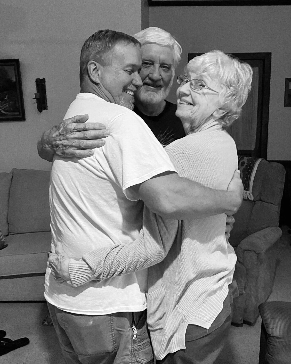 grandparents and their adult son standing together in a hug, arms wrapped around each other while smiling and laughing