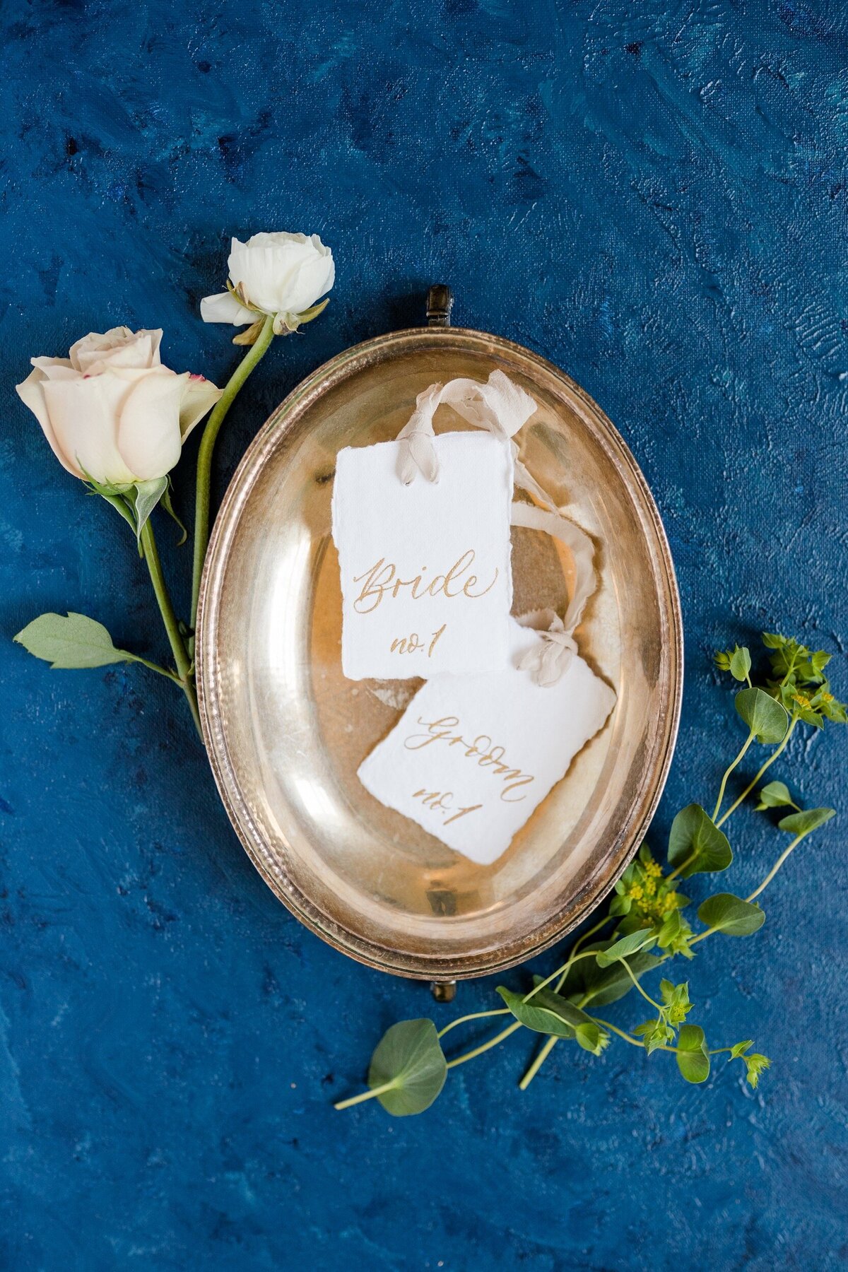 A photo of handmade escort cards for the bride and groom styled in a vintage silver tray on a handpainted blue background at a Charlotte wedding.
