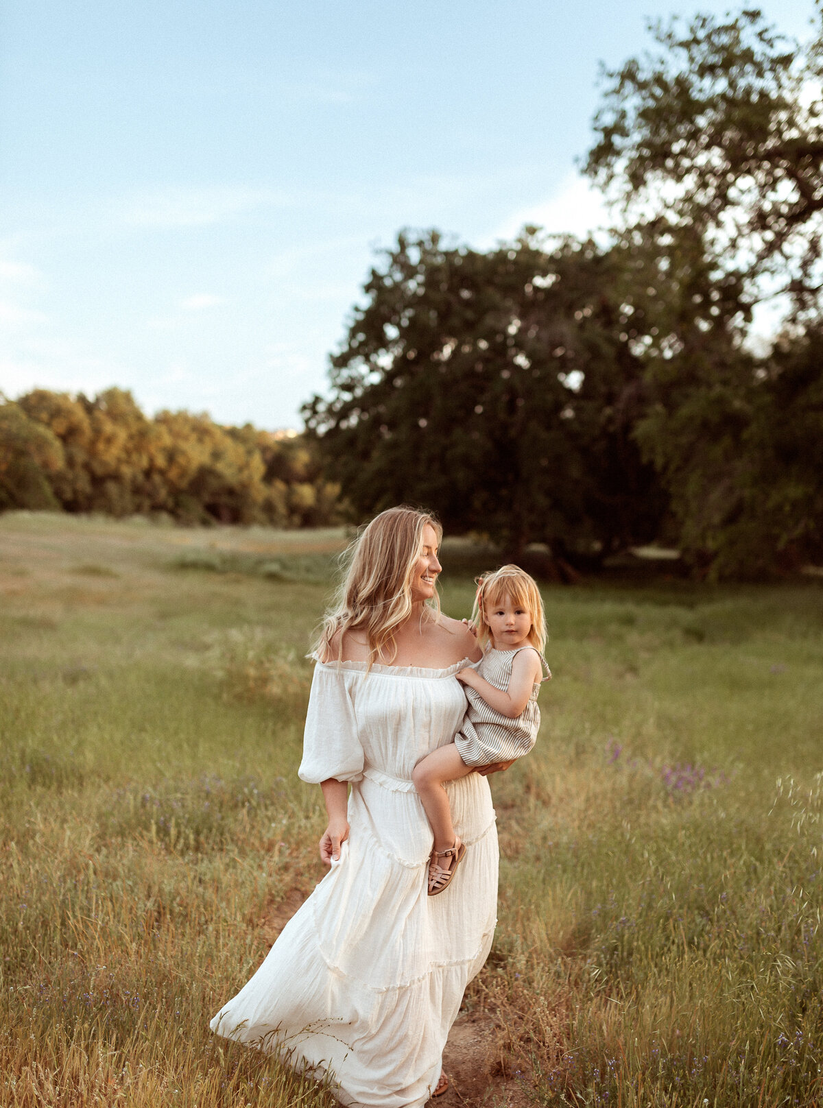 a woman holding her toddler in a field at sunset