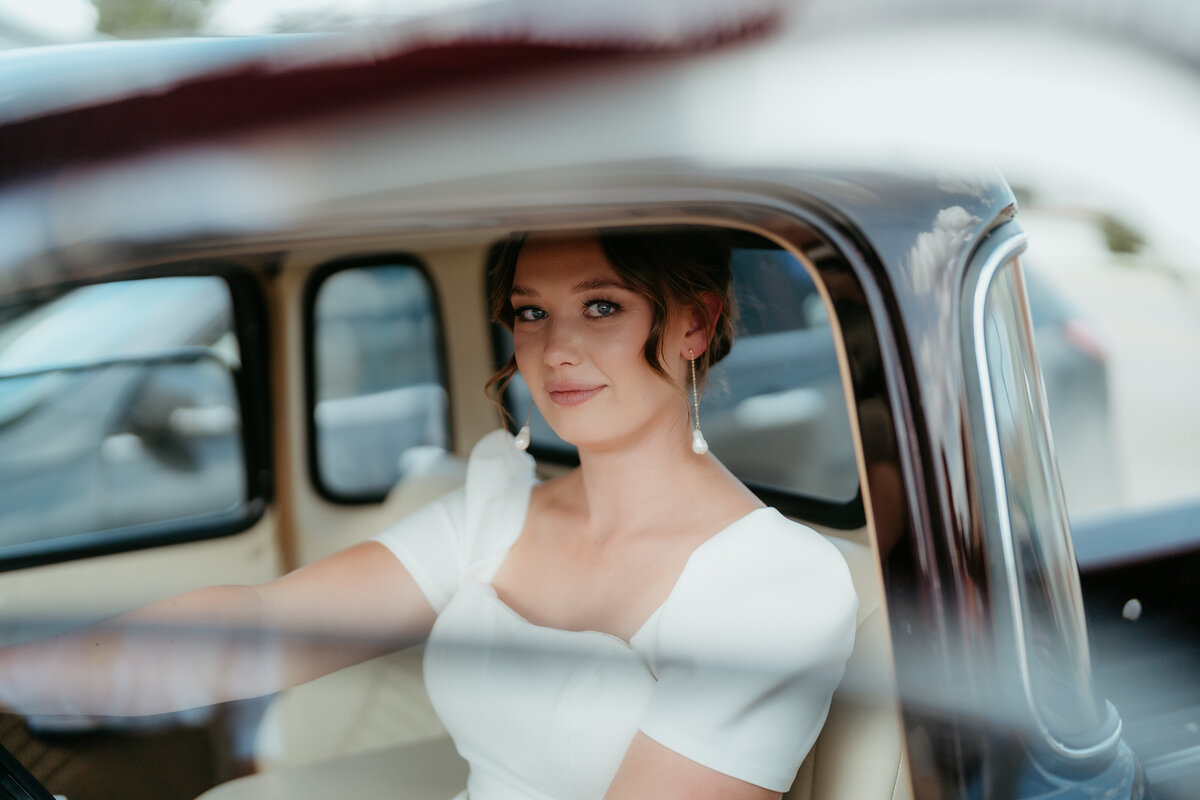 Bride sitting in classic vintage car looking out the window on wedding day.