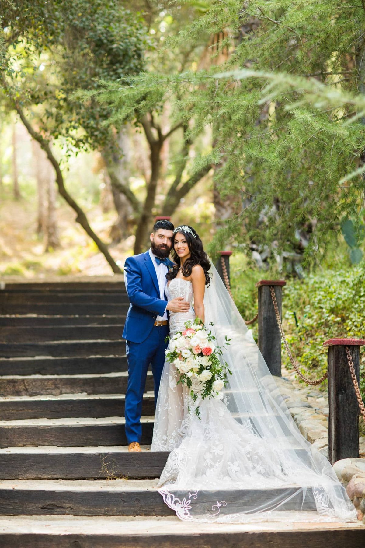 Bride and Groom pose together on an outdoor staircase with the Bride's veil fanned out