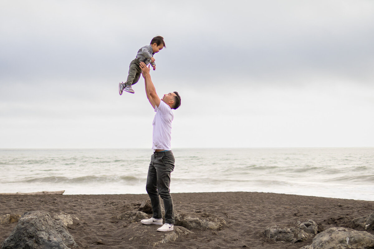 Father lifting his young son in the air with waves in the background, part of Bay Area Maternity Portfolio - Ellobelle Photography