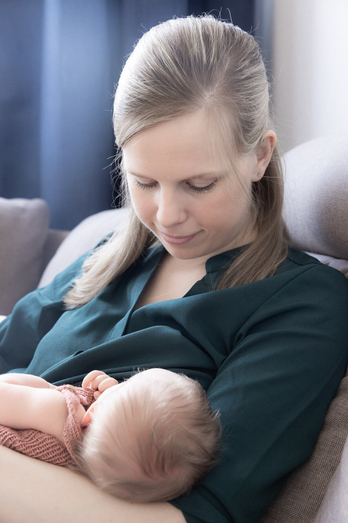 Livsstilsfoto av mor som ammer baby. Mor har grønn bluse på seg og ser på babyen.