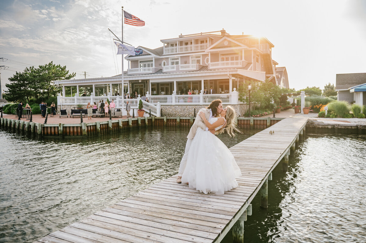 A bride and groom kiss on the dock at Bonnet island Estate during sunset at their summer wedding in New Jersey.