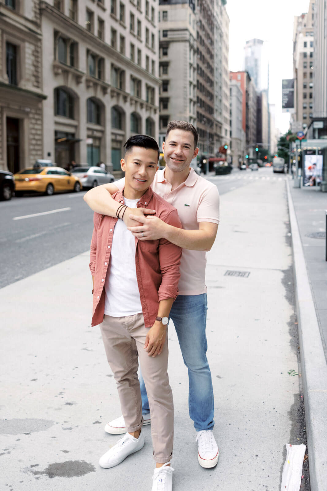 The engaged man is hugging his fiancé from the back, both smiling at West Village, Manhattan, NYC. Image by Jenny Fu Studio.