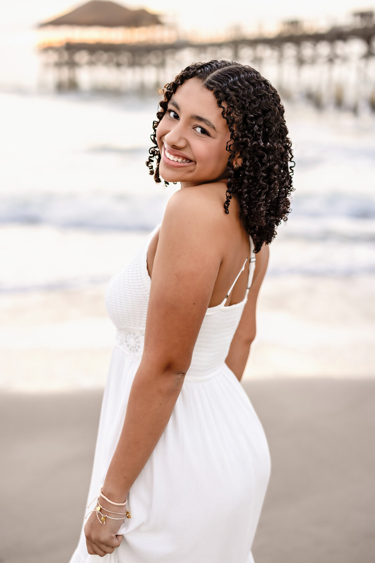 Blue hour senior portraits at Cocoa Beach with a girl in a white dress looking over her shoulder, glowing in soft coastal light.