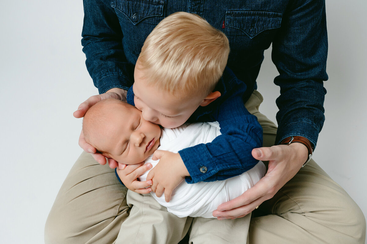 This heartwarming sibling photography session in Pittsburgh, PA captures the sweet moment of an older brother gently kissing his newborn sibling. The natural and intimate shot emphasizes the bond between siblings in their early years.