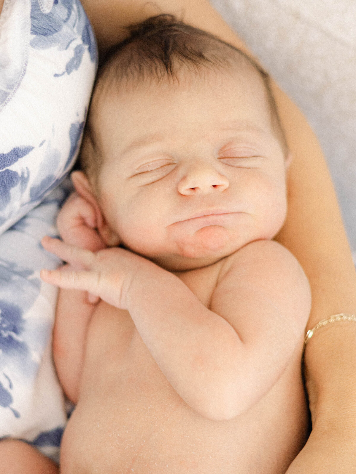 Newborn baby smiling and snuggling his mom's arms.