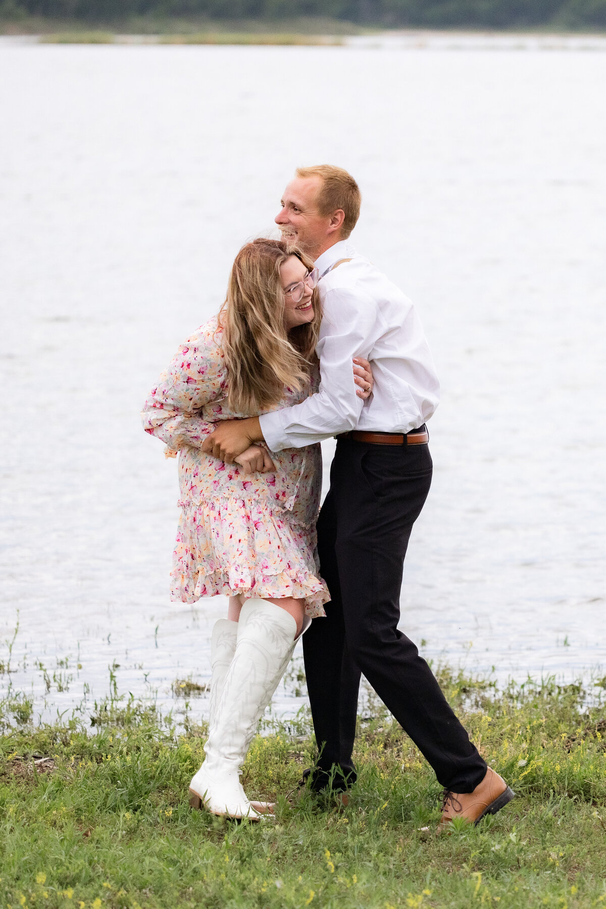 Couple laughing and hugging by the lake with woman in boots