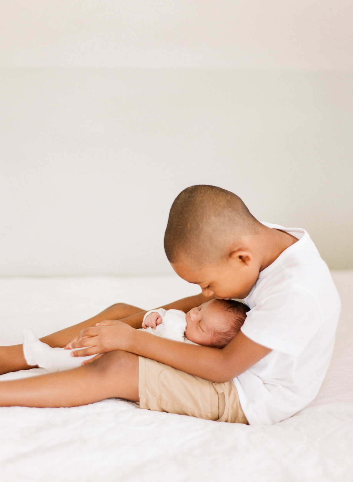 Big brother holds baby brother and kisses him on the head during a Raleigh NC newborn session .Photographed by Raleigh Newborn Photographer A.J. Dunlap Photography.