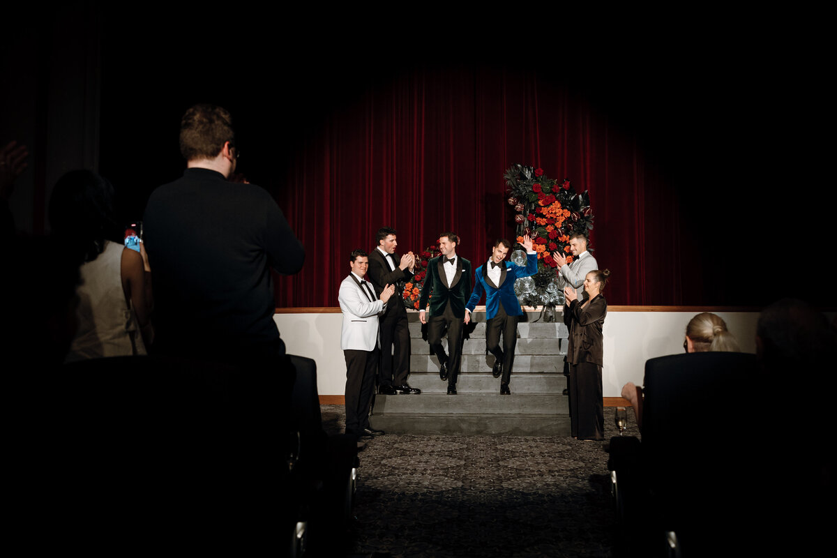 2 grooms exit the stage after wedding ceremony.