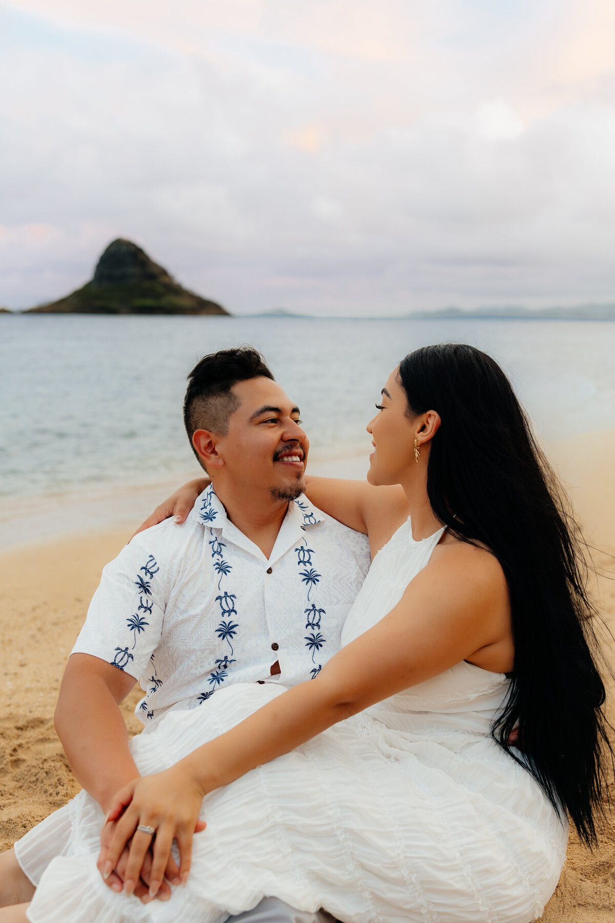 Couple sitting together while embracing during their sunset session at Kualoa Beach in Hawaii