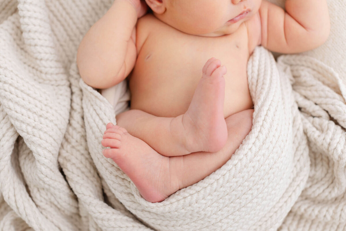 close up image of baby's feet sticking out with a textured beige blanket wrapped around baby's bottom.