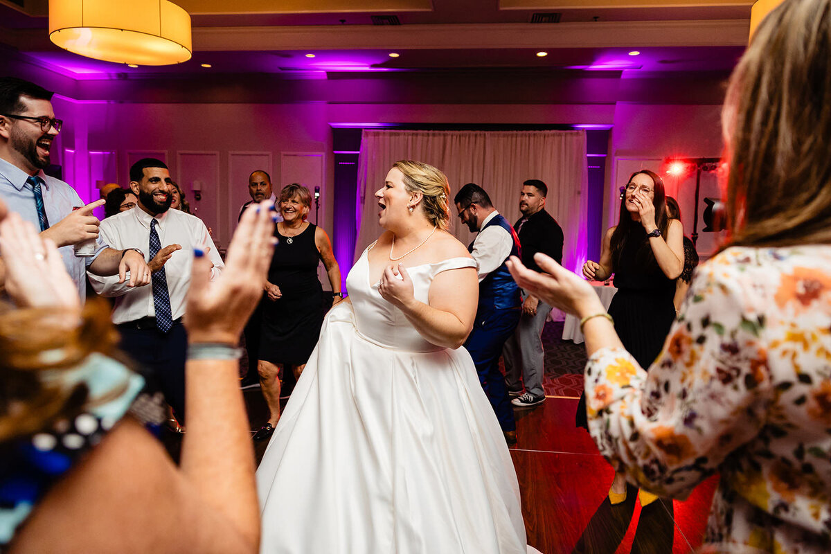A bride encircled by applauding guests enjoys a moment in the spotlight on the dance floor.