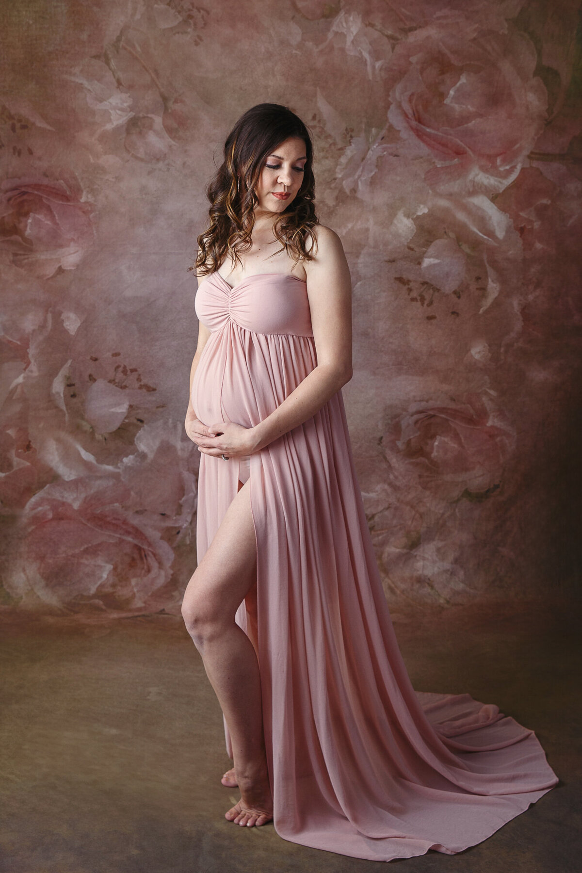 Beautiful pregnant woman wearing a pink maternity gown photographed on a portrait studio background
