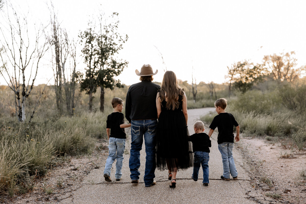 Family of five coordinating in black and denim walking away from the camera. Photo captured by Lubbock family photographer Mary Wiebe