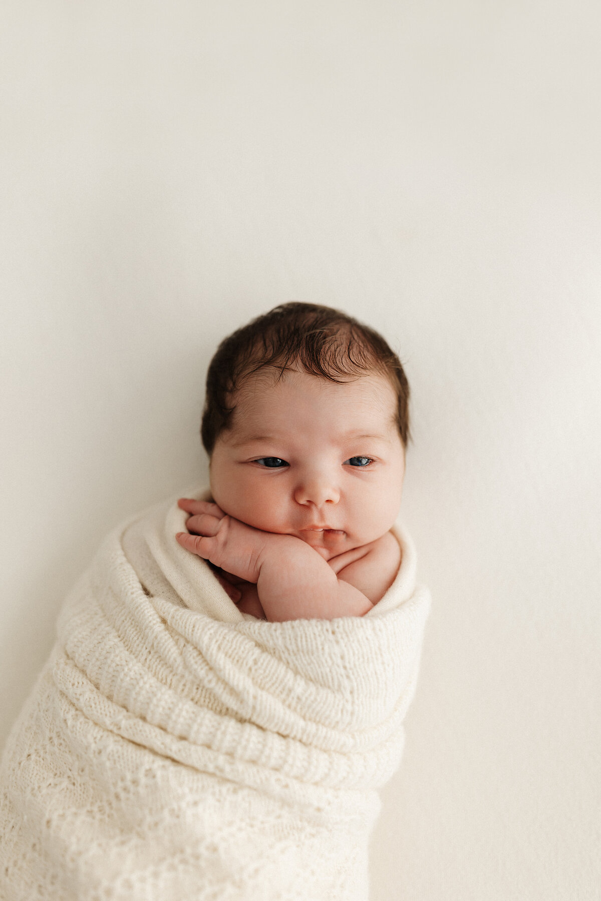Newborn baby wrapped in a white blanket during a newborn studio photoshoot with christchurch newborn photographer lucy jane photography