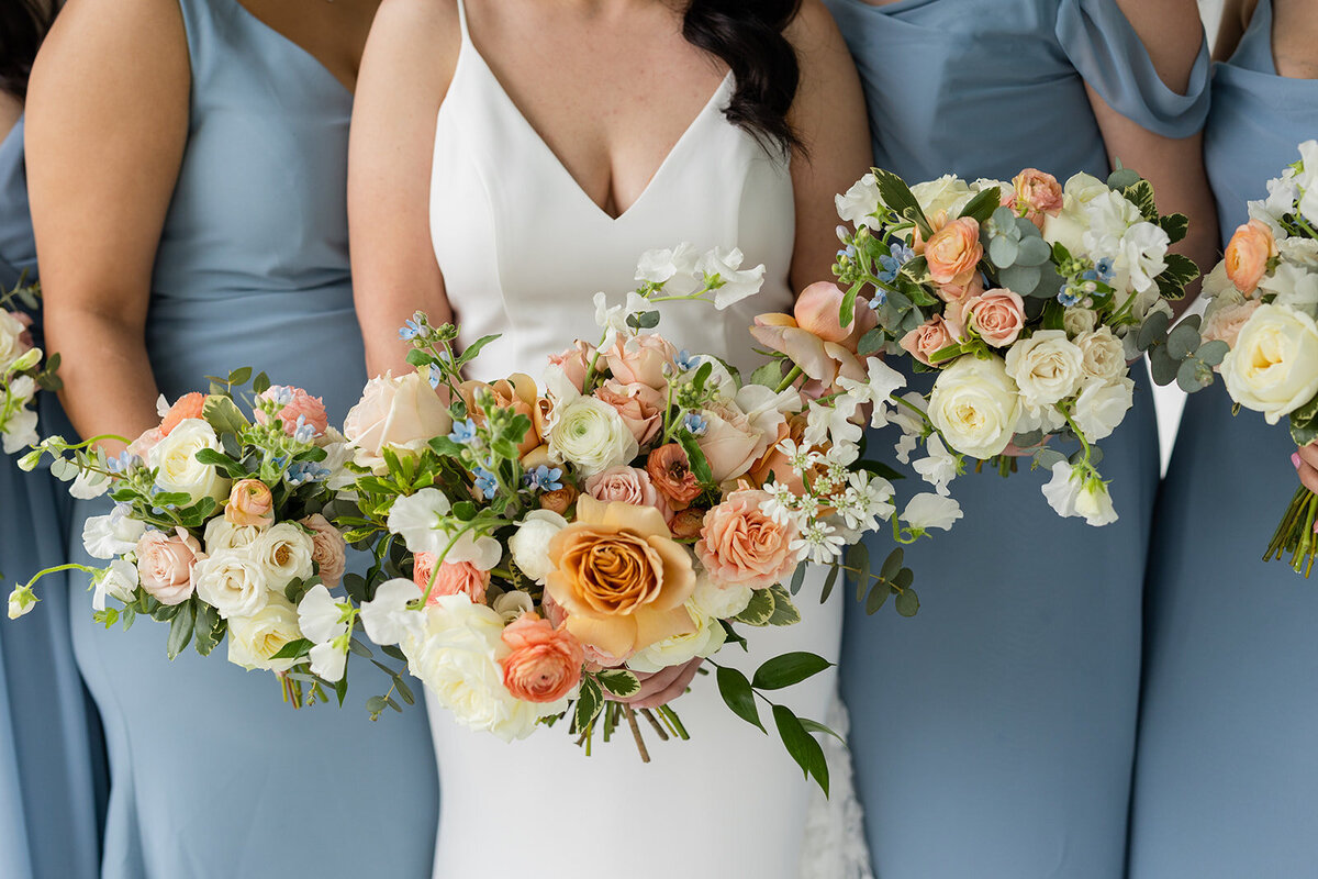 Elegant wedding party holding peach, cream, and blue-toned floral arrangements, crafted for a timeless Texas wedding.
