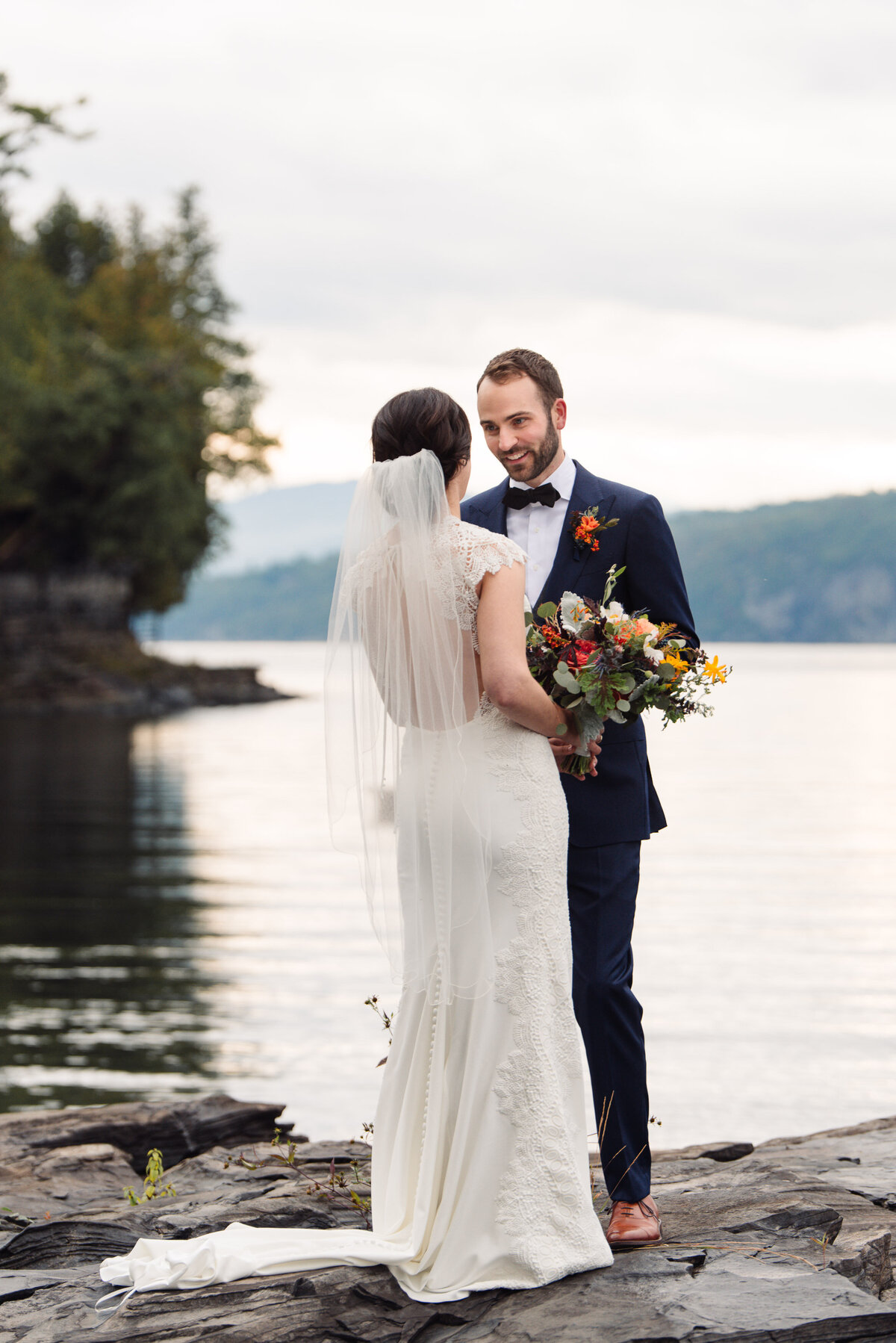 Fall in New England Wedding with couple standing on rocks of the shoreline, with florals by Hollyhocks Flowers in vergennes.