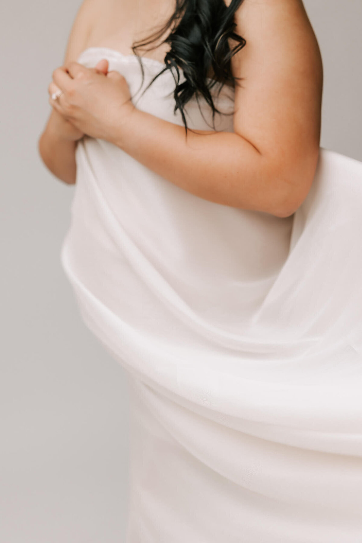 portrait of a woman's pregnant belly and arms. She had the cream silk flowing in the wind and her pregnant belly is outlined.