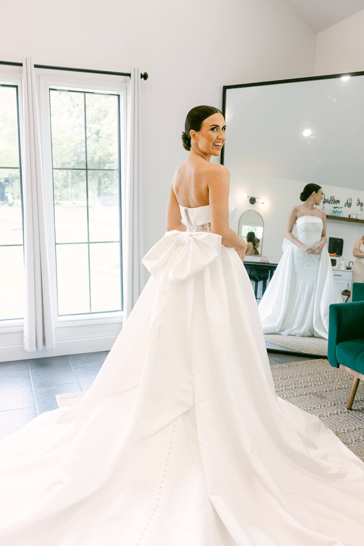 A wedding day photo of the bride in her white dress standing in front of a mirror in her getting ready room