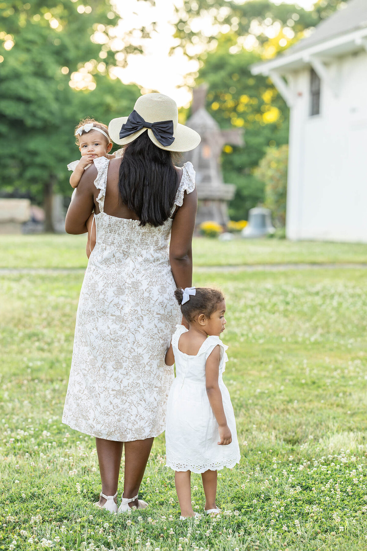 Woman walking forward as she carries her baby and holds her toddlers hand in a clover field of grass