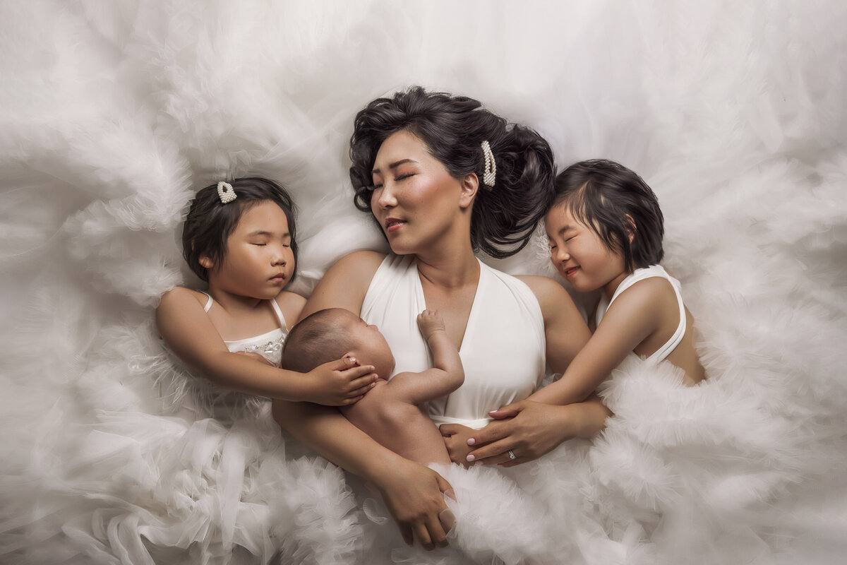 mom and girls of 3 laying down  on white gown near dupont