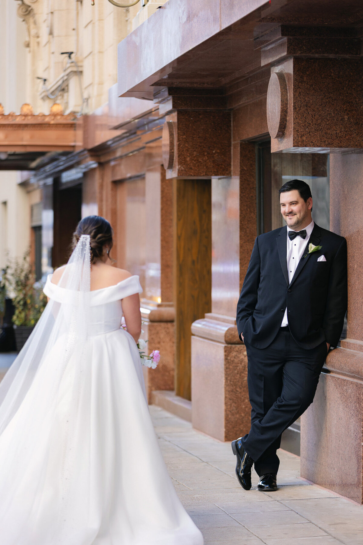 bride and groom outside The Adolphus in Dallas, looking at each other with the groom leaning on a wall, capturing a romantic and intimate wedding portrait.