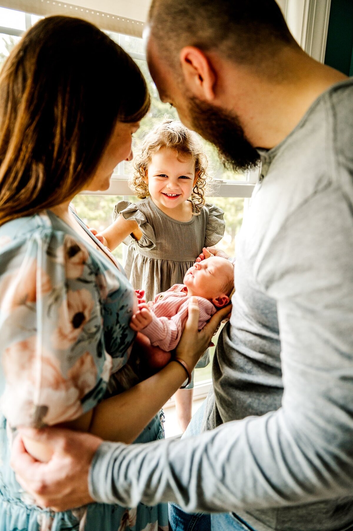 big sister looking at baby being held by mom and dad