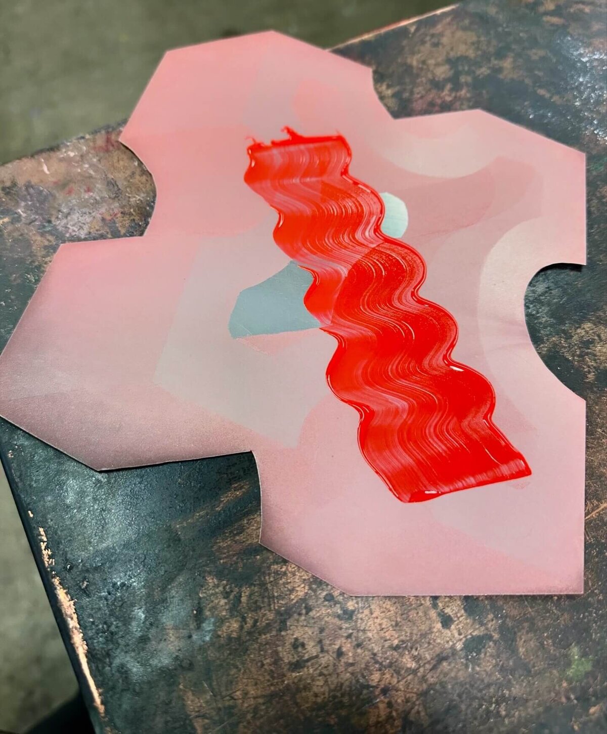 A completed step-etched copper plate inked with red, showing wavy tonal layers across the surface before printing.