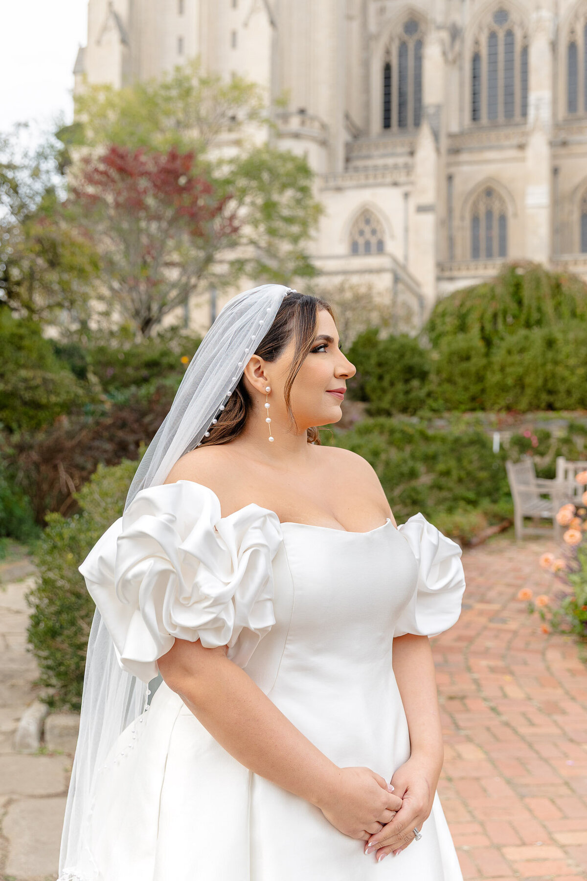 Dressed up in her wedding dress and wearing her veil, a bride stands in front of a gorgeous cathedral in D.C. She's looking to the side at her fiancé (who is standing outside of the frame).