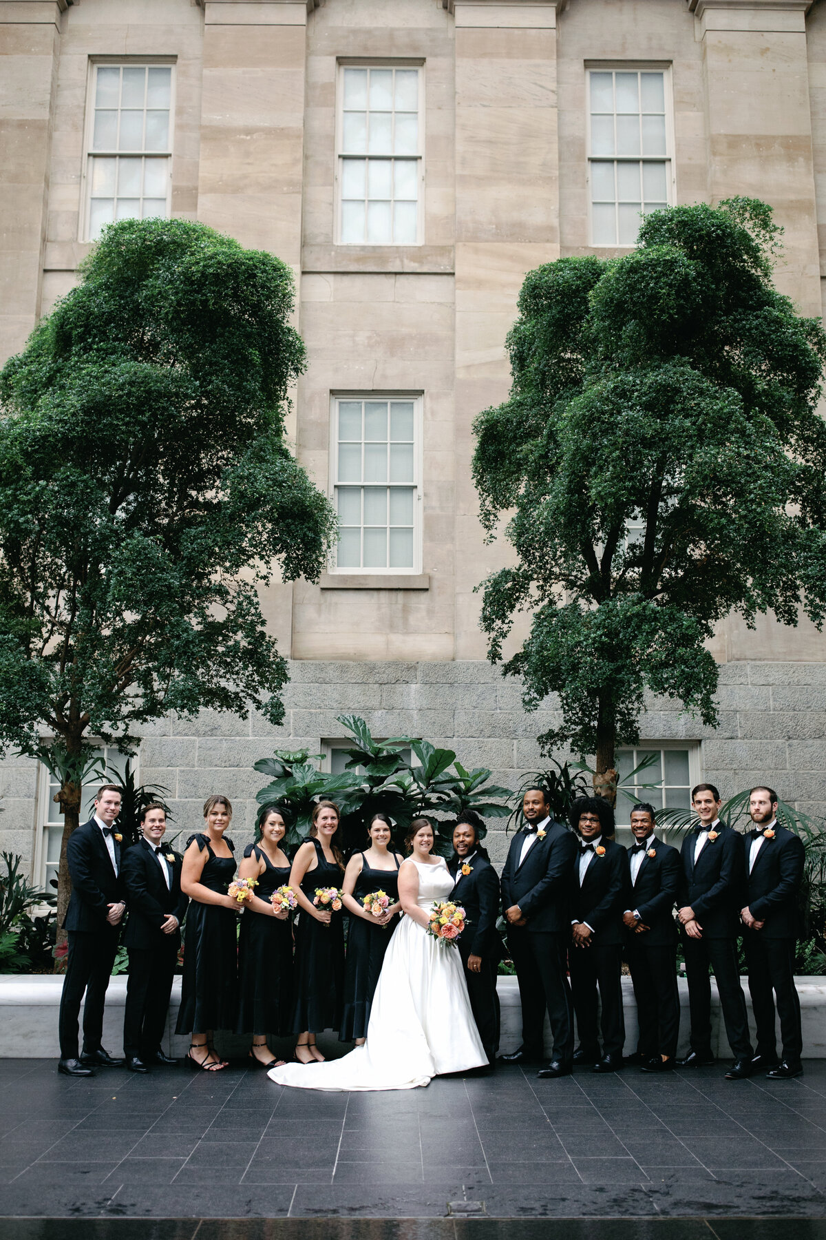 A bride and groom stand inside the National Portrait Gallery with their bridal party with the Coordinative collective. 