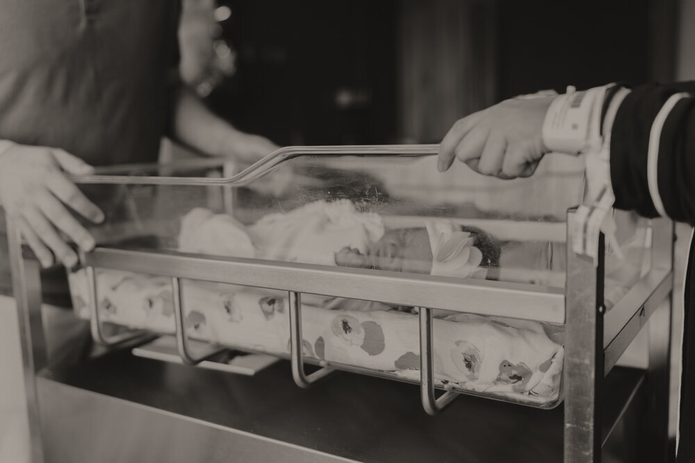 A fresh 48 hospital session in Johnson City, TN. The mother and father are facing each other on each side of the newborn bassinet while the baby lays in the bassinet. 